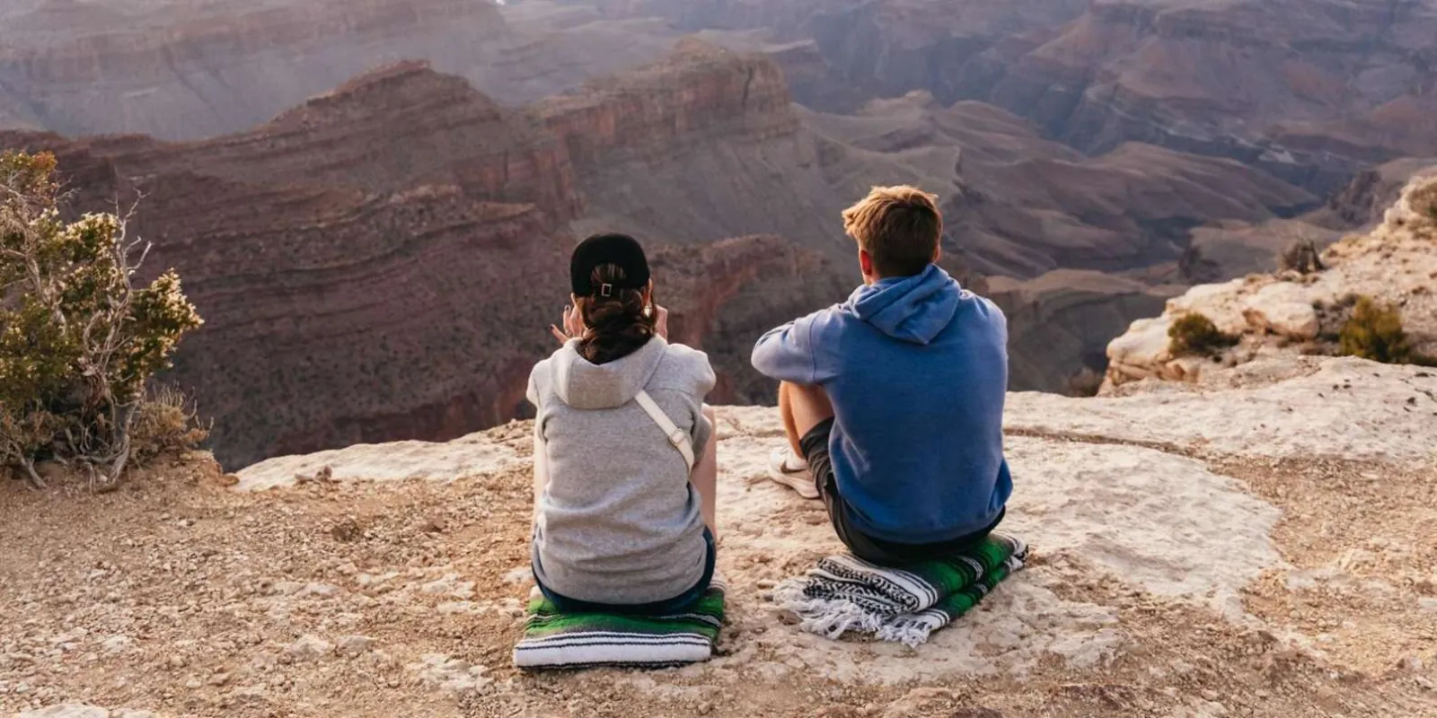 Two visitors sitting at the South Rim edge taking in the mile-deep canyon