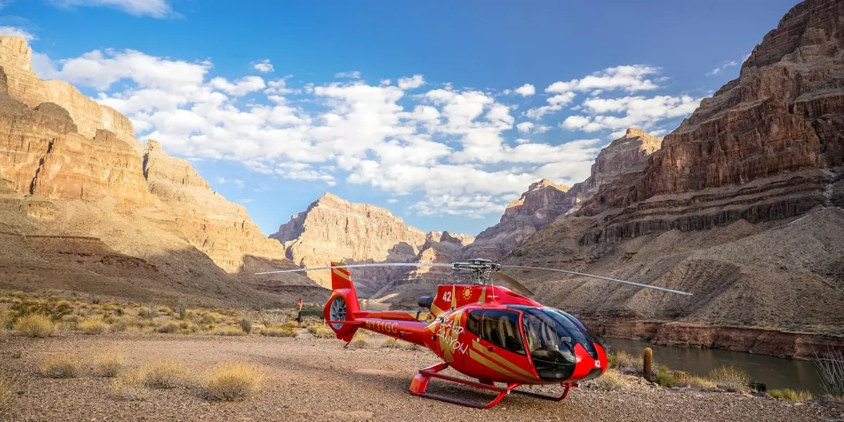 Red Papillon EcoStar helicopter parked on the canyon-floor landing site beside the Colorado River