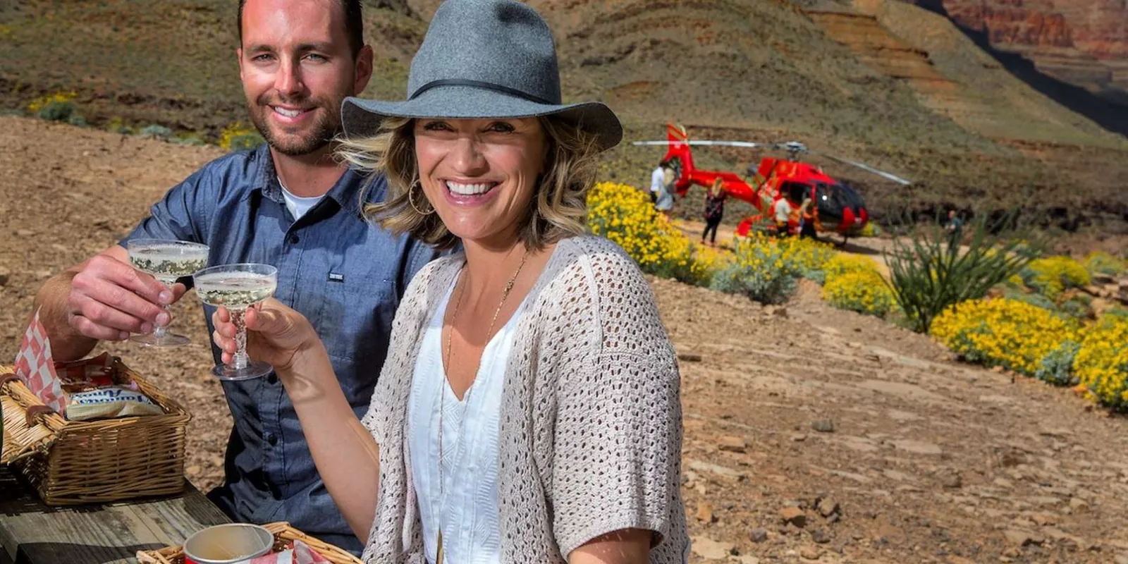 Couple toasting with champagne at the canyon-floor picnic stop, helicopter parked behind